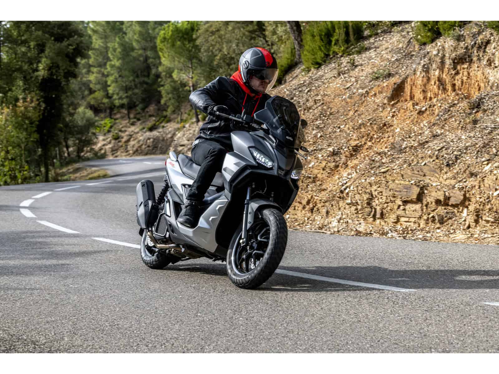 Motorradfahrer auf kurvenreicher Straße Ein Motorradfahrer fährt auf einer kurvenreichen Straße. Der Fahrer trägt eine schwarze Jacke und einen schwarzen Helm mit roten Akzenten.