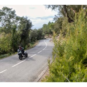 Motorradfahrer auf einer kurvenreichen Landstraße Ein Motorradfahrer fährt auf einer kurvenreichen Straße durch eine grüne Landschaft. Der Fahrer trägt Schutzkleidung.
